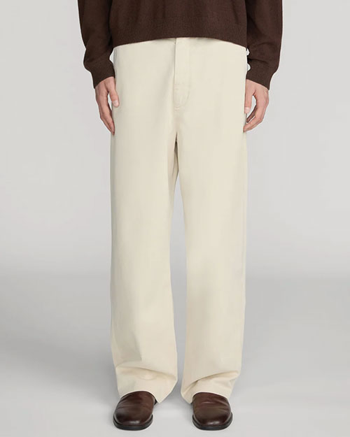 Front view of cream-colored wide-leg trousers with a relaxed fit, flat front, and full-length legs that drape over dark brown leather shoes. The trousers are shown from the waist to the feet and are paired with a dark brown knit top against a light gray background.