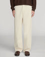 Front view of cream-colored wide-leg trousers with a relaxed fit, flat front, and full-length legs that drape over dark brown leather shoes. The trousers are shown from the waist to the feet and are paired with a dark brown knit top against a light gray background.