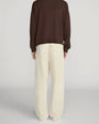 Back view of cream-colored wide-leg trousers with a relaxed fit and full-length legs that fall loosely to the floor. The trousers are paired with a dark brown long-sleeve knit top and shown from the shoulders to the feet against a light gray background.