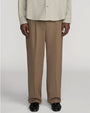 Front view of taupe straight-leg trousers with a relaxed fit and pressed front creases. The trousers are shown from the waist to the feet and are styled with a light beige textured button-front shirt and black leather shoes against a light gray background.