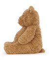 Side view of a plush teddy bear with light brown, fluffy fur, sitting upright. The bear’s rounded ears, arms, and legs are visible, and its profile shows a slightly protruding snout.