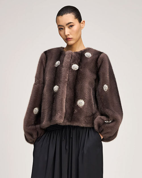 Brown fur-textured jacket with a collarless neckline, voluminous sleeves, and pearl-like floral embellishments throughout, paired with a black gathered skirt.