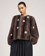 Brown fur-textured jacket with a collarless neckline, voluminous sleeves, and pearl-like floral embellishments throughout, paired with a black gathered skirt.