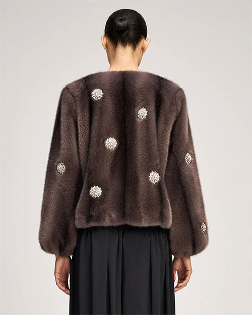 Brown fur-textured jacket with a collarless neckline, voluminous sleeves, and pearl-like floral embellishments throughout, paired with a black gathered skirt.