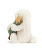 Plush white rabbit toy with long ears, sitting and holding a green plush Christmas tree topped with a gold star.