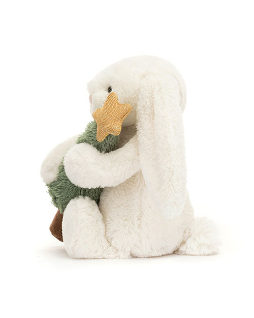 Plush white rabbit toy with long ears, sitting and holding a green plush Christmas tree topped with a gold star.