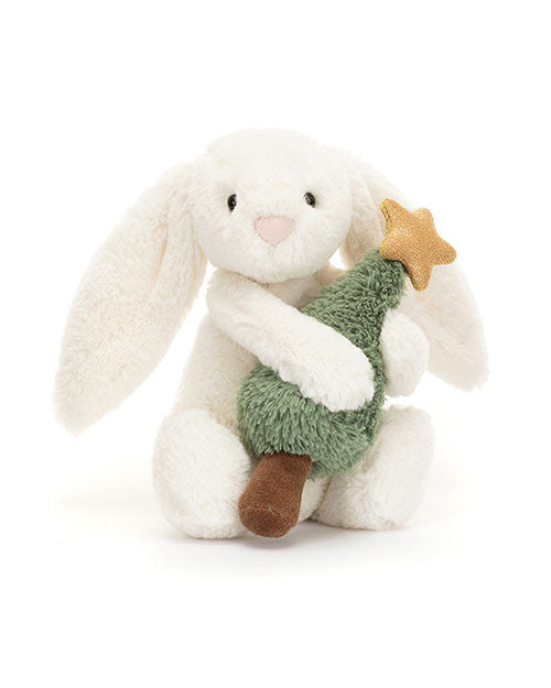 Plush white rabbit toy with long ears sitting upright and hugging a small green plush Christmas tree topped with a golden star.