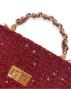Close-up of a small rectangular burgundy tweed handbag embellished with sequins, featuring a gold-tone twist-lock closure and a braided top handle with chain links.