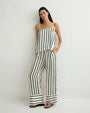 Person modeling a loose, cream-colored camisole and wide-leg pants set with vertical green stripes, hands in pockets, paired with black sandals against a plain light background.