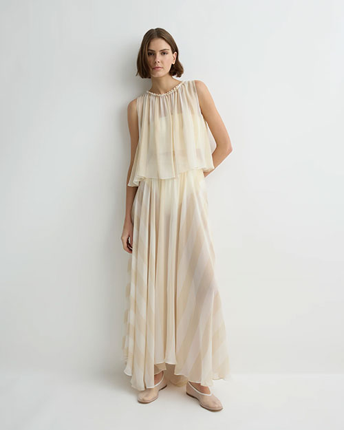 Close-up of a person wearing a soft cream sleeveless top with a gathered neckline and layered, flowy fabric, paired with a matching skirt against a plain light background.