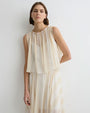 Close-up of a person wearing a soft cream sleeveless top with a gathered neckline and layered, flowy fabric, paired with a matching skirt against a plain light background.
