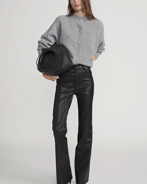 Person wearing a light gray button-up cardigan with a round neckline, paired with high-waisted black leather pants and holding a large black handbag.