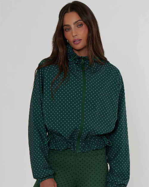 Model wearing a dark green zip-front jacket with a subtle dotted pattern and gathered waist detail against a light background.