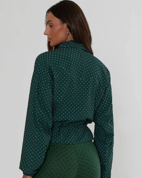 Model wearing a dark green zip-front jacket with a subtle dotted pattern and gathered waist detail against a light background.