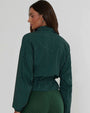 Model wearing a dark green zip-front jacket with a subtle dotted pattern and gathered waist detail against a light background.