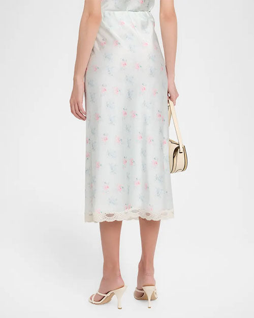 Rear view of a light green floral top with thin straps, lace-trimmed V-neck bodice, fitted silhouette, and midi-length hem, styled with a small top-handle bag and sandals.