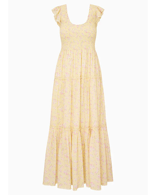 A light yellow, ankle‑length dress with a soft floral pattern in pastel tones. The dress features a smocked bodice, a scoop neckline with ruffled edges, and short flutter sleeves. The skirt is tiered with subtle gathered seams, creating a flowing, airy silhouette.