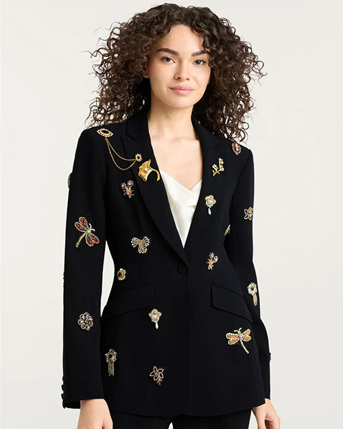 Black tailored blazer adorned with multiple ornate embroidered and jeweled embellishments, including dragonflies, flowers, and decorative motifs in gold, red, and metallic tones. The blazer is worn over a white V-neck top.