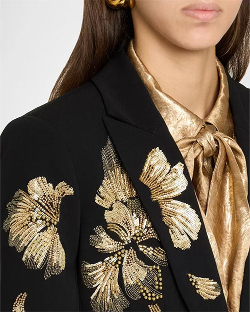 Black tailored blazer with gold floral embroidery on the front and sleeve, styled over a metallic gold tie-neck blouse.