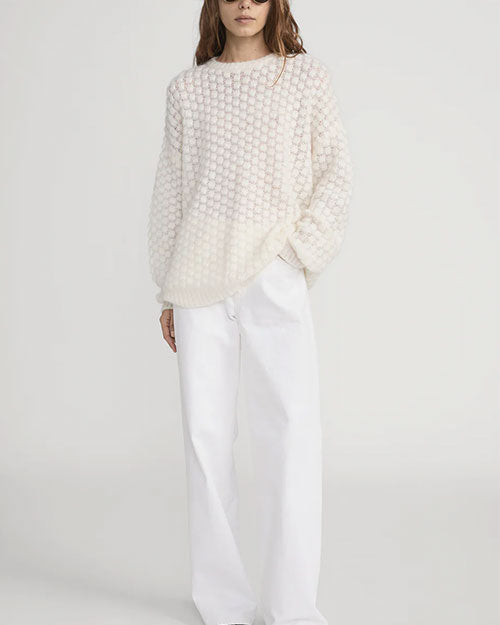 Person wearing a textured cream-colored long-sleeve sweater with a raised bubble-knit pattern, paired with loose-fitting white pants. The sweater has a relaxed fit and a round neckline.