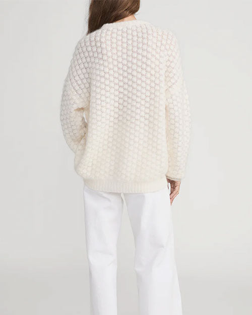 Back view of a person wearing a cream-colored textured bubble-knit sweater with long sleeves and a ribbed hem, paired with loose-fitting white pants. The sweater has a relaxed fit and a round neckline.