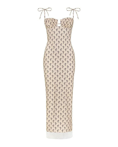 A sleeveless, cream-colored maxi dress with thin shoulder tie straps and a fitted silhouette. The dress features a small black floral print pattern throughout and a subtle cut-out detail at the bust. The hemline reaches the ankles.