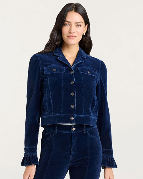 “Front view of a person wearing a dark blue velvet jacket with button closure, flap chest pockets, and ruffled cuffs, paired with matching velvet pants.”