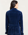 Back view of a person wearing a dark blue velvet jacket with structured seams and buttoned cuffs, paired with matching high-waisted pants featuring back pockets.