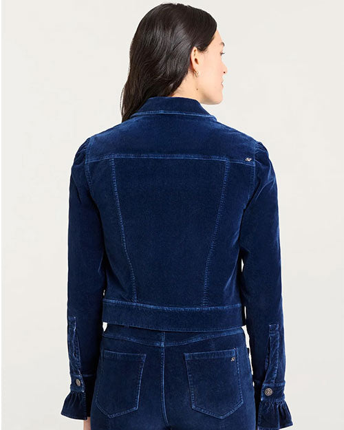 Back view of a person wearing a dark blue velvet jacket with structured seams and buttoned cuffs, paired with matching high-waisted pants featuring back pockets.