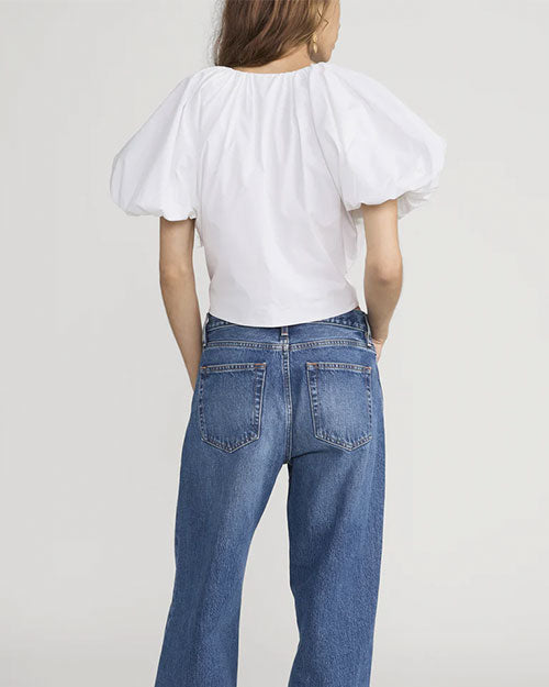 Back view of a person wearing a white short-sleeve blouse with voluminous puff sleeves. The blouse is paired with high-waisted blue jeans.