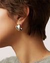 Close-up of an ear wearing a chunky, polished silver hoop earring with a sculptural, rounded design.