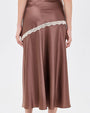 Close-up of a mauve satin midi skirt with contrast ivory lace trim in an asymmetrical diagonal panel, creating a flowing, slip-inspired silhouette.