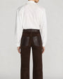 Back view of a white long-sleeve blouse tucked into high-waisted dark brown pants. The blouse features a pointed collar, a relaxed fit, and sleeves gathered at the cuffs. The pants have a suede-like texture, a wide waistband with belt loops, and large back patch pockets with contrasting leather-look trim. The straight-leg silhouette falls cleanly to the hem. The outfit is shown against a light gray background.
