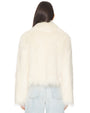 Back view of a person wearing a white faux fur jacket with a long, shaggy texture. The jacket has a slightly cropped length and is paired with light blue denim jeans. The hair is straight and falls down the back, partially covering the collar area of the jacket.