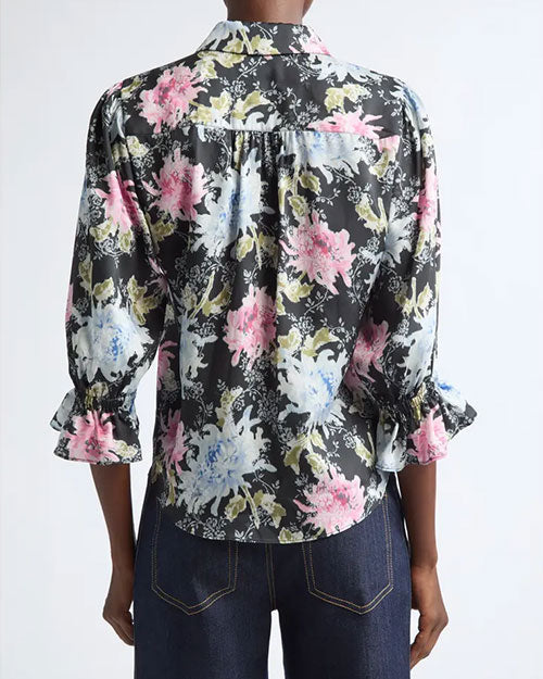 Black button-front blouse with a painterly floral print in pink, white, and green, featuring a pointed collar and three-quarter sleeves with ruffled cuffs.