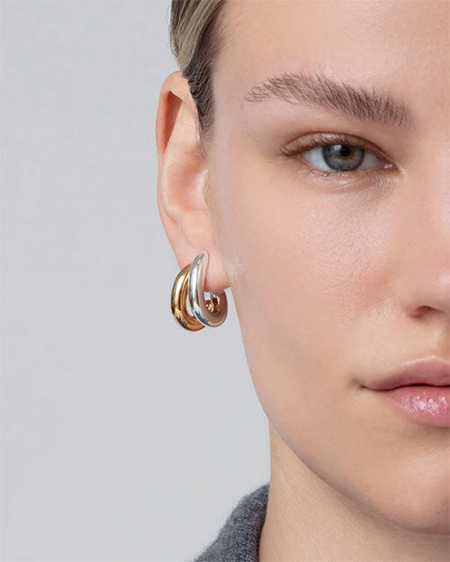 Close-up of an ear wearing a thick, polished gold hoop and silver earring with a smooth, rounded finish.