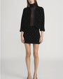 Model wearing a black textured two-piece outfit consisting of a cropped jacket and a mini skirt, both embellished with small pearl-like beads. The jacket has three-quarter sleeves and an open front, paired with a sheer black top underneath.