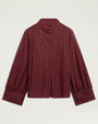 Product image of a burgundy long-sleeve blouse with a subtle metallic striped texture, band collar, hidden button-front closure, and voluminous sleeves with wide buttoned cuffs. The blouse is shown laid flat against a light gray background.
