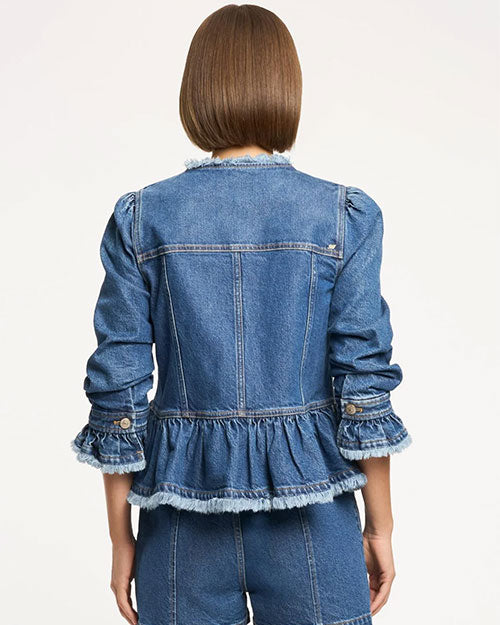 Back studio view of a cropped denim peplum jacket featuring vertical seam detailing, gathered waist flounce, frayed trim along the hem and collar, and long sleeves with ruffled cuffs, shown against a light neutral background.