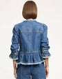 Back studio view of a cropped denim peplum jacket featuring vertical seam detailing, gathered waist flounce, frayed trim along the hem and collar, and long sleeves with ruffled cuffs, shown against a light neutral background.