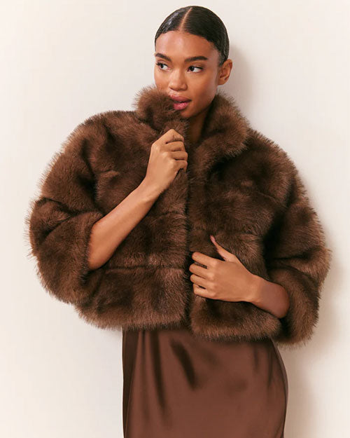 Front view of an outfit featuring a cropped brown faux fur jacket with a plush, textured finish, styled over a floor-length satin slip dress in a matching brown tone.