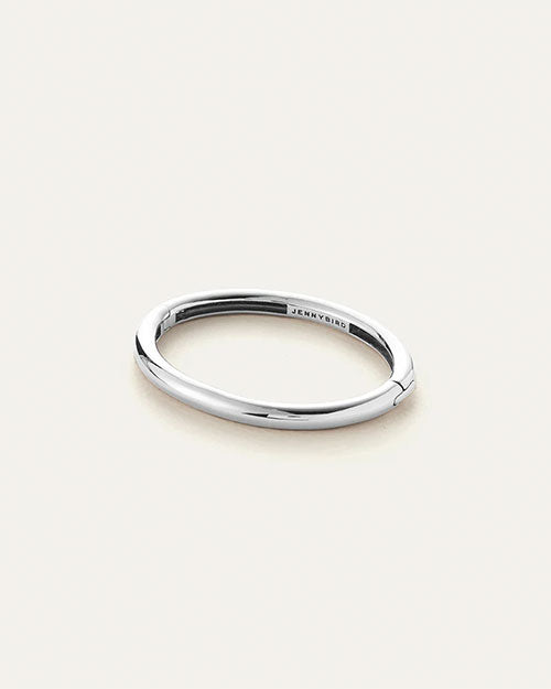 Polished silver oval-shaped bracelet with a smooth, minimalist design and hinge closure, engraved with the brand name ‘Jenny Bird’ on the inner side.