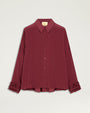 Product image of a burgundy button-front blouse with a pointed collar, long sleeves, and a relaxed silhouette. The blouse features ruffled cuff detailing, tonal buttons, and a slightly curved hem with an extended back panel. Shown laid flat against a light gray background.