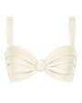 A cream-colored bikini top with thick shoulder straps and softly ruched cups. The fabric is gathered toward the center, where a small knotted detail creates a twist effect. The overall design is structured, minimal, and symmetrical, with smooth, matte material and clean stitching.