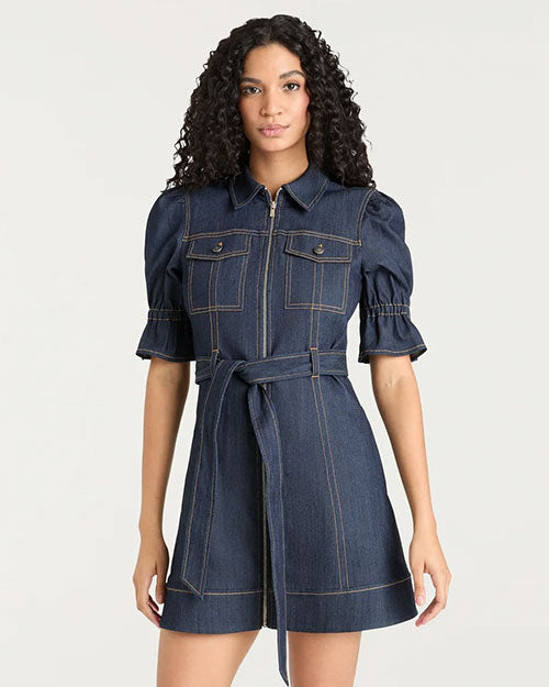 Front view of a dark denim mini dress featuring short puff sleeves, a pointed collar, front zipper closure, chest flap pockets, contrast topstitching, and a self-tie belt at the waist, photographed against a light studio background.