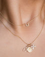 Two layered gold necklaces with delicate chains. The upper necklace has a diamond-studded horseshoe pendant, while the lower necklace features multiple charms, including a horseshoe, an eye medallion, and a four-leaf clover, all adorned with small diamonds.