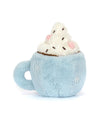 Plush toy shaped like a light blue cup of hot chocolate with a handle on the left side, topped with white whipped cream, brown chocolate sprinkle-like pieces, and pink marshmallow-like accents. The toy has a soft, fuzzy texture and a cozy, whimsical design.