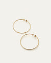 Pair of large, thin gold hoop earrings with a simple, minimalist design, displayed on a light neutral background.