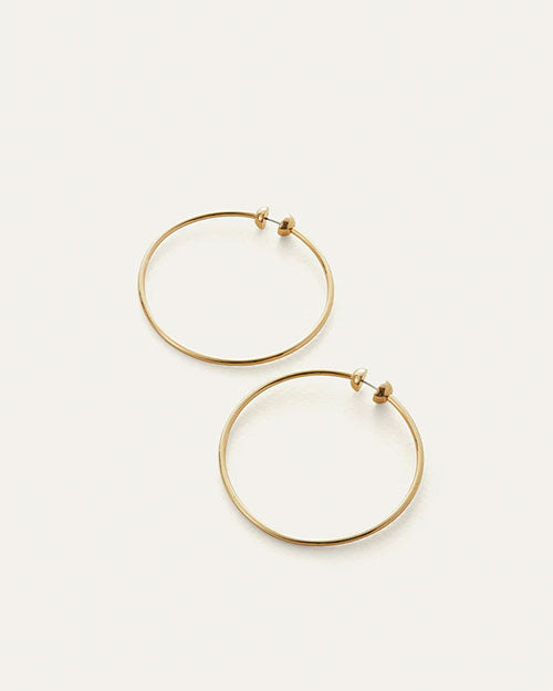 Pair of large, thin gold hoop earrings with a simple, minimalist design, displayed on a light neutral background.
