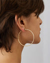 Close-up of an ear wearing a large, thin gold hoop earring, with short brown hair framing the ear.
